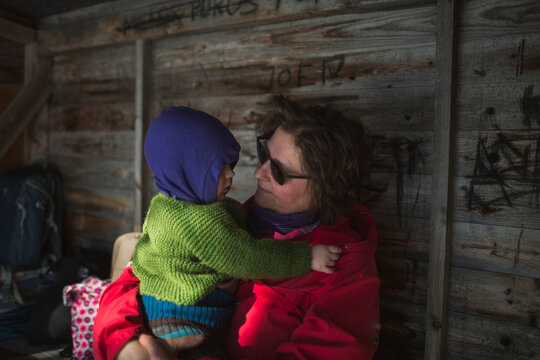 Mother spending leisure time with baby boy wearing warm clothing in log cabin