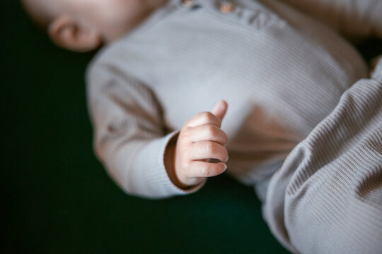 Tiny hand of newborn toddler wearing ribbed outfit while lying down on couch
