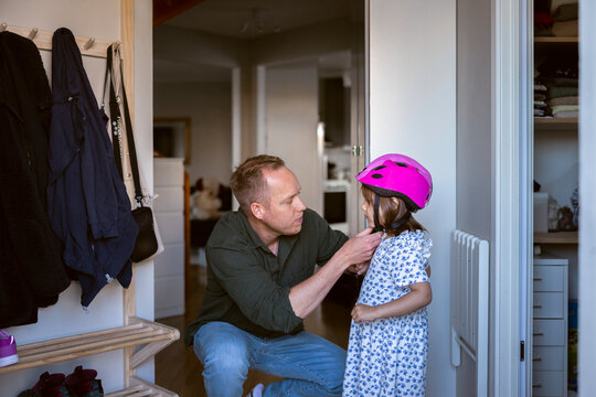 Father adjusting cycling helmet strap of her daughter before bike ride