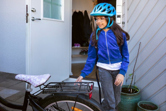 Girl wearing helmet and walking towards her cycle outside house