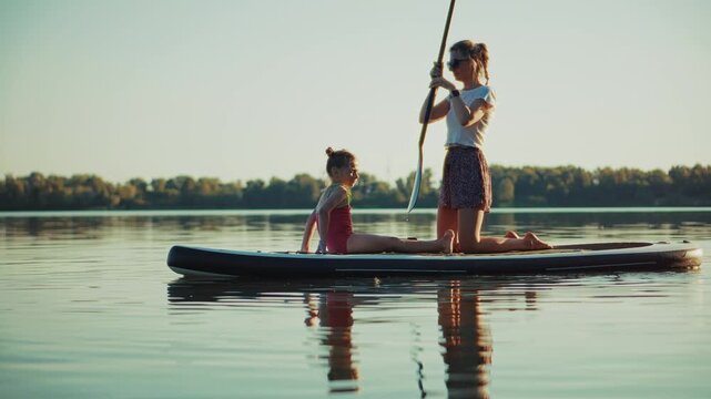 Paddleboarder With Child On Stand Up Paddle Board Paddling On Lake