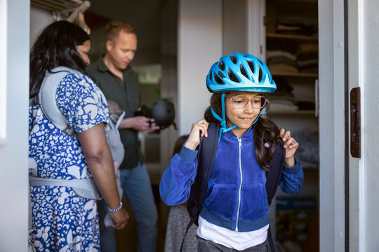 Girl with backpack getting ready to leave house with parents in background