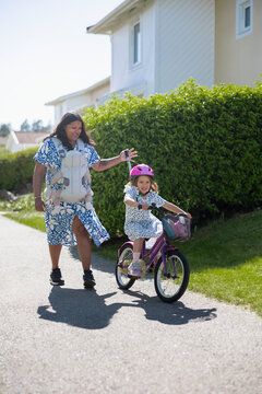 Smiling woman wearing baby carrier and guiding her daughter's bike on path