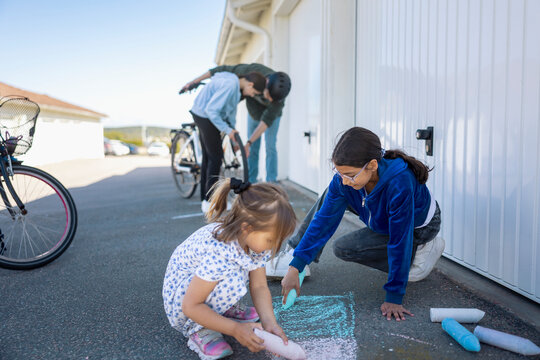 Sisters drawing with large pieces of chalk on driveway
