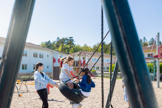 Sisters having fun while playing on tire swing in playground