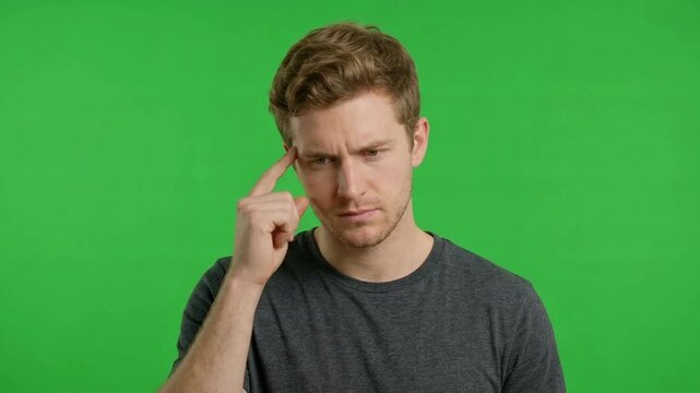 A young man thoughtfully contemplating with a neutral expression against a bright green background