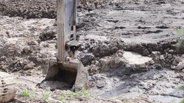 Raw industrial energy and relentless earth-moving force dominate the scene; dark, clumped soil and rugged machinery convey heavy labor and extraction
