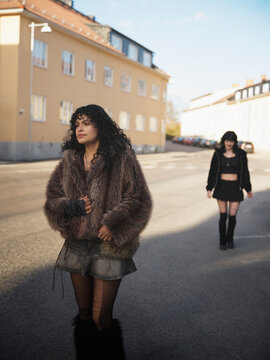Fashionable woman in fur coat walking on road with her girlfriend in background