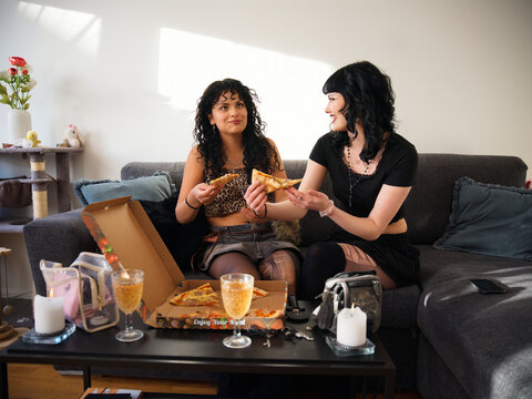 Happy lesbian couple spending leisure time eating pizza while sitting on sofa at home
