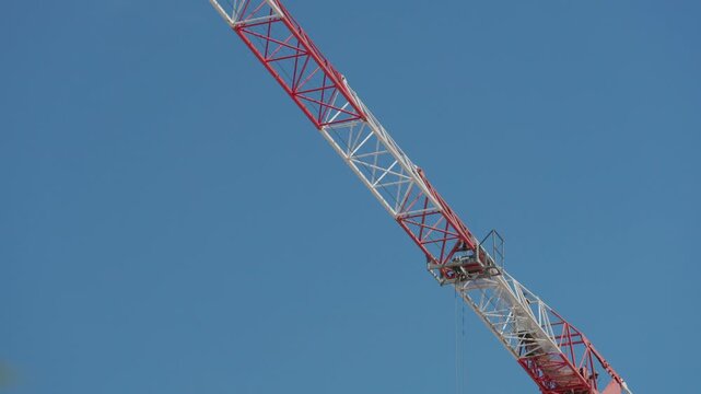 Large red and white crane jib is lifting cargo at a construction site against a clear blue sky
