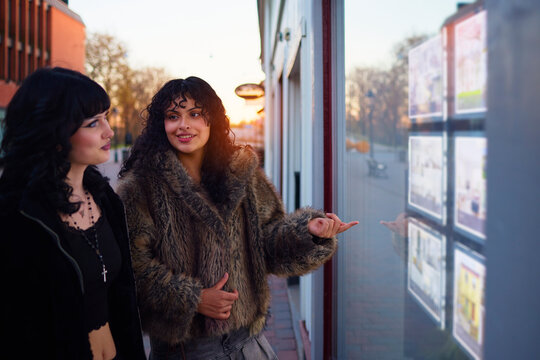 Lesbian woman pointing at store window while discussing with girlfriend during shopping