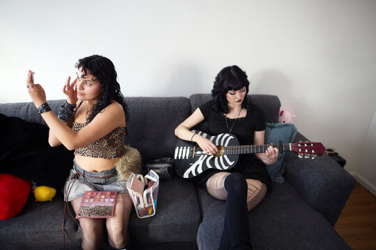 Lesbian woman applying make-up while her partner playing guitar sitting on sofa
