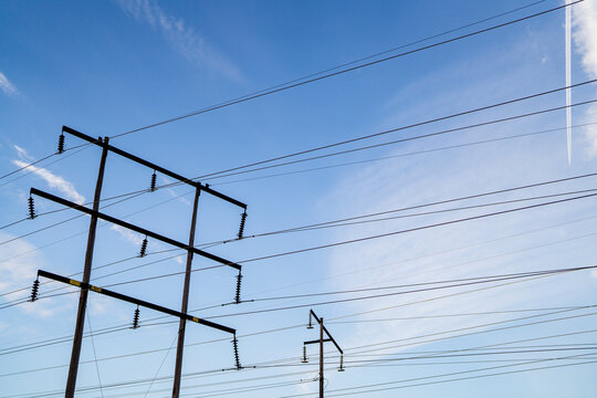 Tall utility poles with numerous parallel power lines stretching across bright blue sky