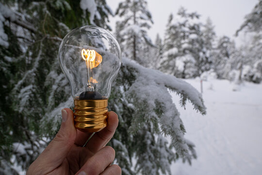 Hand of unrecognizable person holding light bulb with glowing filament against snowy forest