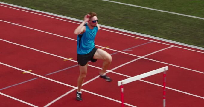 High angle view captures athlete stepping over hurdle on running track. Concept of athletics practice, obstacle training, coordination and summer sports preparation.