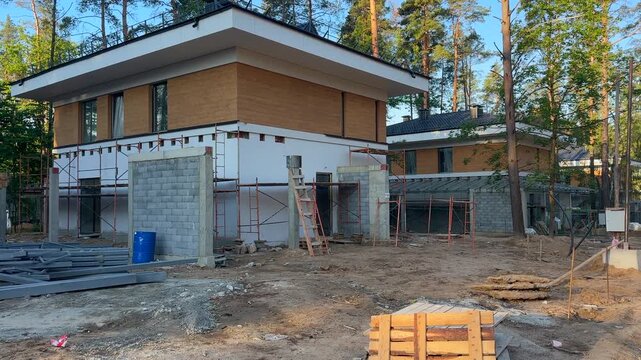 Construction of new home in forest. Scaffolding for fa&ccedil;ade work. Housing development outside city. Building modern double court house. Construction of family house in suburb. Dream modern home 