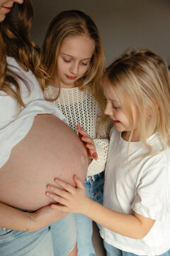 Siblings touching pregnant mother's belly while feeling unborn child movements at home