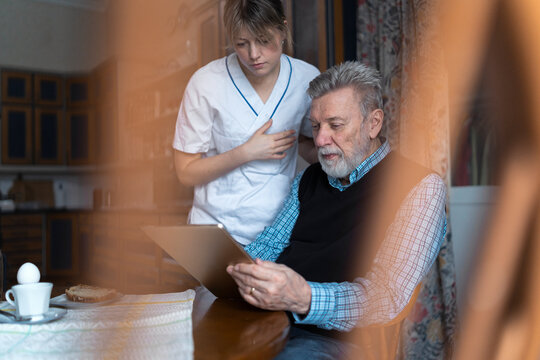 Female caregiver assisting elderly man using digital tablet while sitting for breakfast at home