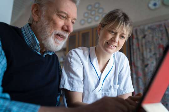 Smiling female visiting nurse assisting senior patient in using wireless technology at home