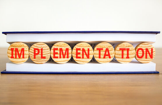 Implementation word symbol. Concept word Implementation on beautiful wooden circles in book. Beautiful wooden table white background. Business implementation word concept. Copy space.