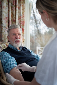 Senior man talking with female nurse applying bandage on his arm during house call