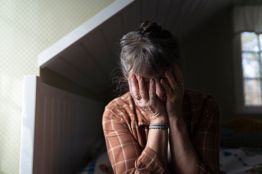 Mature woman sitting with hands covering face in bedroom at home