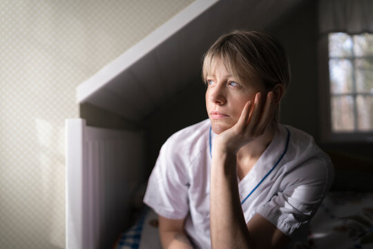 Contemplative nurse looking away while leaning on elbow in bedroom