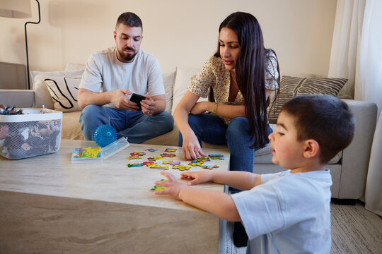 Man using smart phone while woman making jigsaw puzzle with son at home