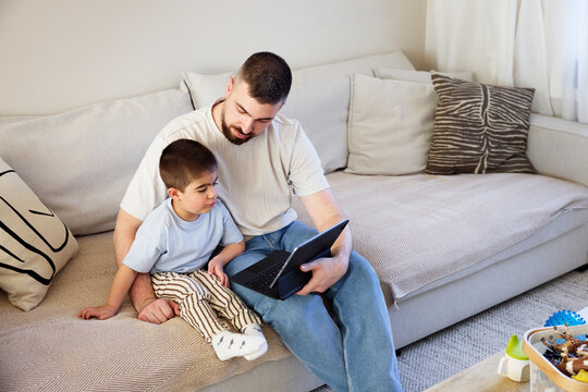 High angle view of father showing videos on laptop to son while sitting at home