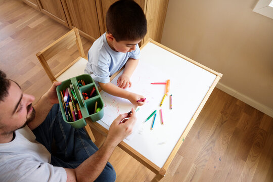 High angle view of father sitting with son coloring on paper at table in home