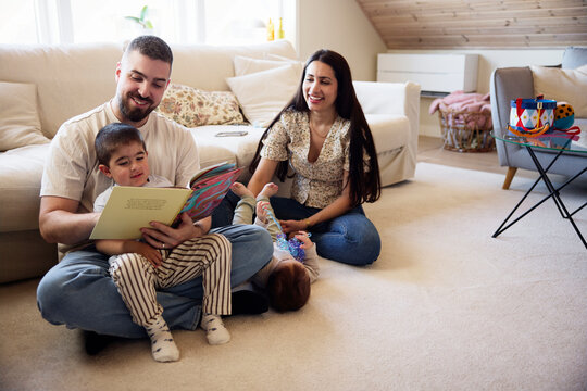 Smiling parent looking at son reading picture book while sitting in living room at home