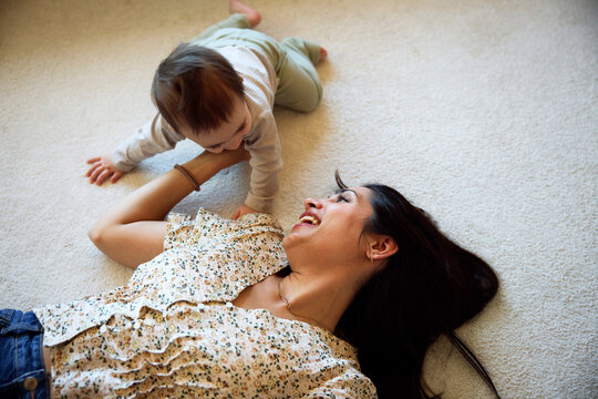 High angle view of happy mother playing with male toddler while lying on carpet in living room