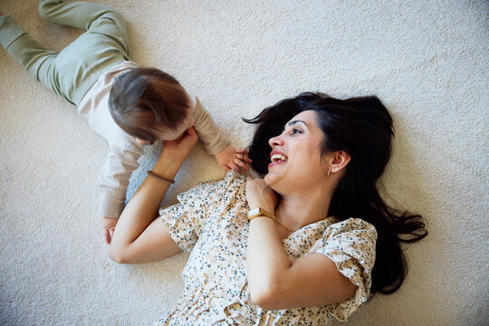High angle view of happy mother playing with male toddler while lying on carpet at home