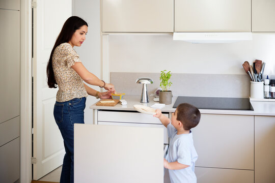Boy passing plate to mother making breakfast in kitchen at home