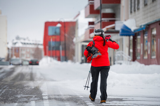 Rear view of female skier walking on snow covered road with equipments in winter