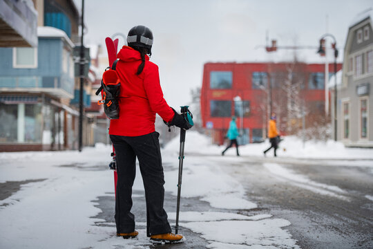 Rear view of female skier standing with ski pole on snow covered road at street in winter