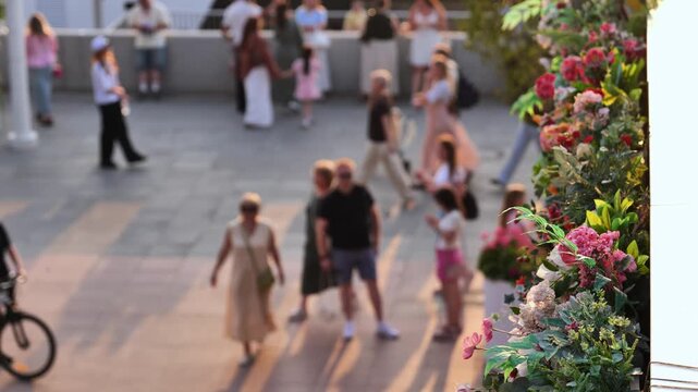 Blur of people walking on sunny street with blooming flowers