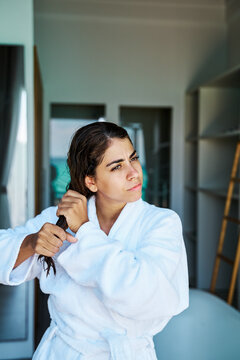 A white woman combs her wet hair indoors in a bathroom in a home