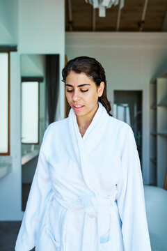 A woman relaxes wearing a white bathrobe indoors in a home