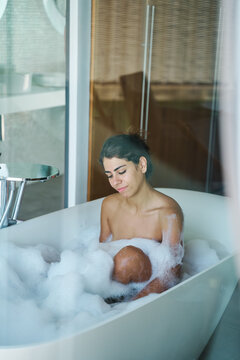 A white woman relaxes in a bubble bath inside a modern bathroom