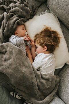 Directly above view of sibling sleeping with pacifier on bed at home