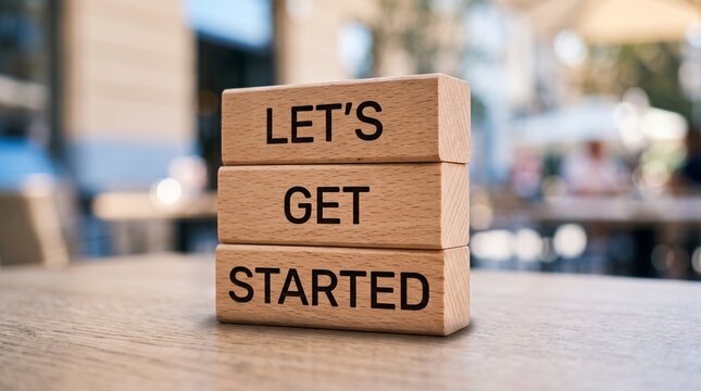 Wooden blocks with motivational message let&rsquo;s get started on desk with blurred office background
