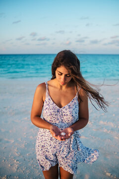 A white woman holding a seashell on a beach by the ocean in a beach