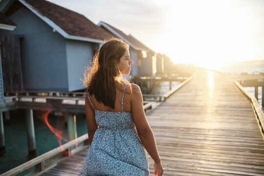 A white woman walks along a boardwalk by overwater bungalows
