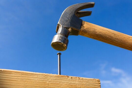 Claw hammer above nail in wooden plank against blue sky
