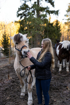 Female caretaker petting horse while standing in muddy field