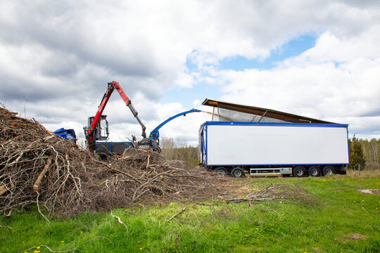 Tractor utilizing hydraulic crane arm to load tree branches into chipper mechanism against cloudy sky
