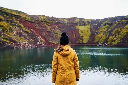 A white woman in a yellow jacket stands by a volcanic crater lake