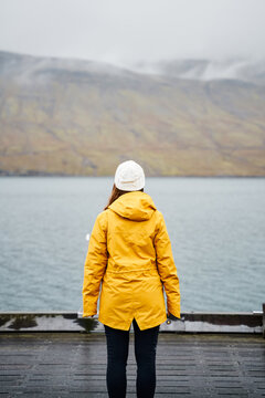 A white woman in a yellow jacket stands on a dock overlooking a misty