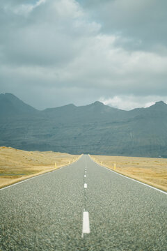 A straight road leads through grassy fields toward mountains
